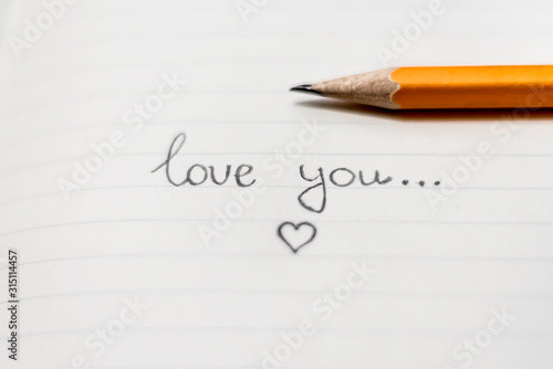 A pencil is on the lined paper. A lettering Love you and little drawing heart. Space for text. Concept of Saint Valentine's Day.