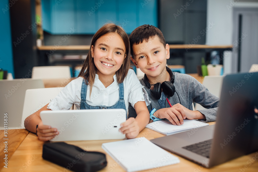 Two happy small friends writing homework , using smart digital tablet at modern blue classroom. Two happy small friends writing homework , using smart digital tablet at modern blue classroom.