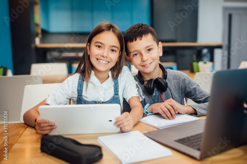 Two happy small friends writing homework , using smart digital tablet at modern blue classroom. © Тарас Нагирняк