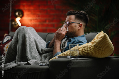 Young sick man sitting on sofa.