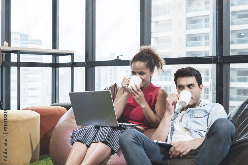 couple using laptop, holding a cup and smiling while sitting on beanbag chairs couple using laptop, holding a cup and smiling while sitting on beanbag chairs
