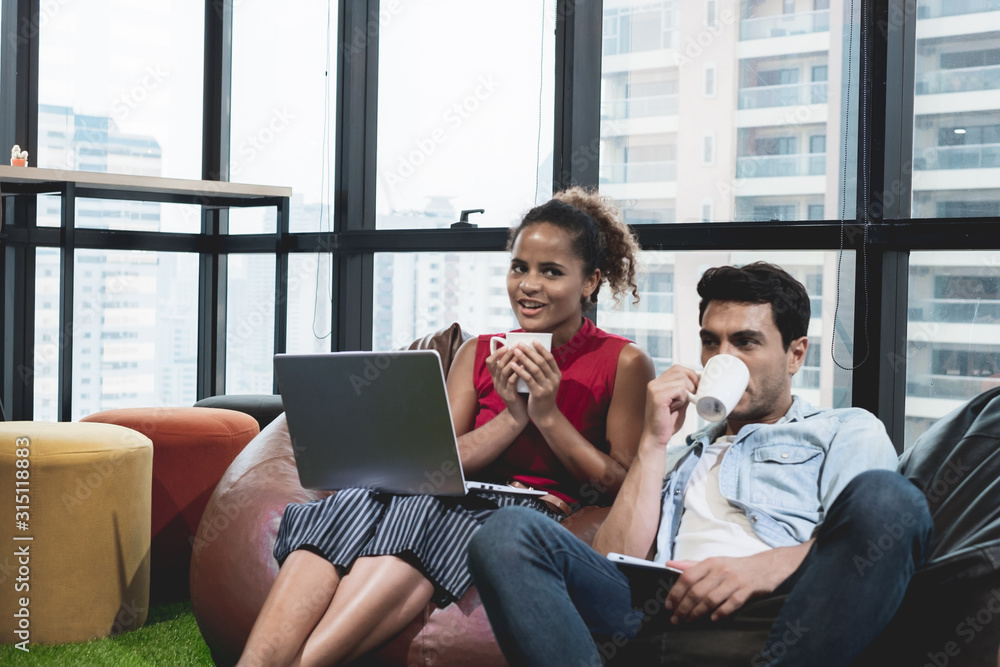 couple using laptop, holding a cup and smiling while sitting on beanbag chairs couple using laptop, holding a cup and smiling while sitting on beanbag chairs