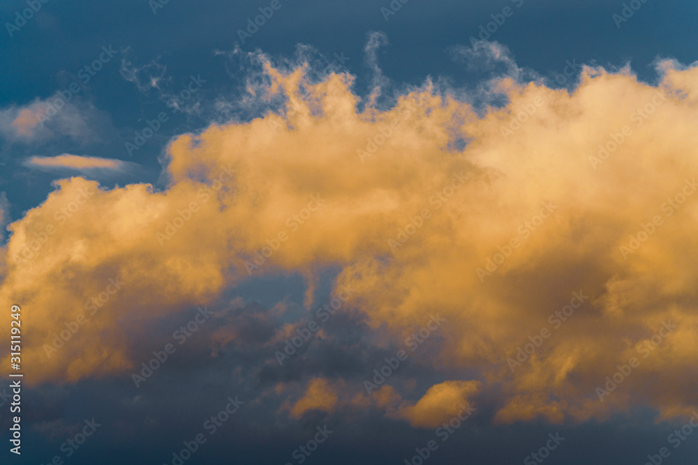 Beautiful golden fluffy clouds illuminated by disappearing rays at sunset, thunderclouds floating across sunny blue sky to change season weather. Natural abstract meteorology background.