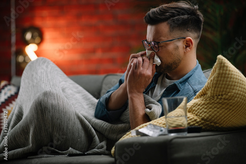 Young sick man sitting on sofa.