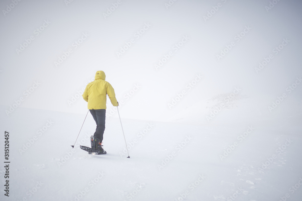 Athlete man dressed in yellow walking through the snow with snowshoes, there is a lot of fog, the horizon is not visible Athlete man dressed in yellow walking through the snow with snowshoes, there is a lot of fog, the horizon is not visible