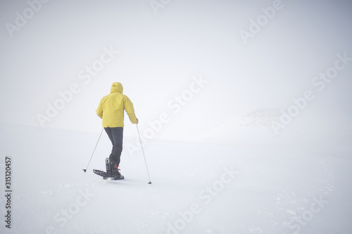Athlete man dressed in yellow walking through the snow with snowshoes, there is a lot of fog, the horizon is not visible