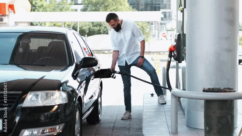 A man is at the gas station. He is filling up his car with petrol. The ...