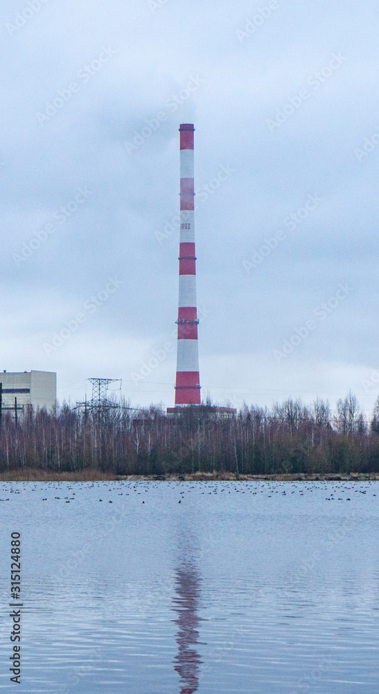 Red-white factory chimney near a winter lake.