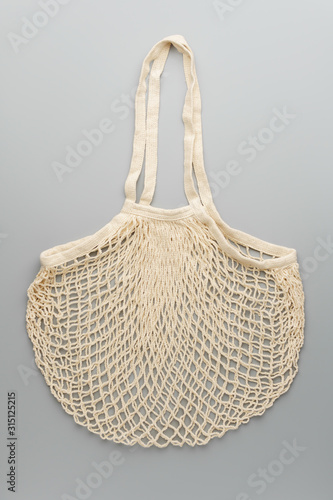 Zero waste concept. A reusable white mesh shopping bag lies on gray background. Vertical orientation, top view.