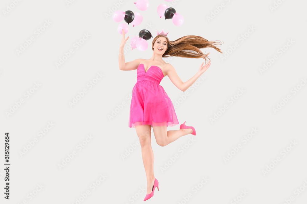 Jumping young woman in beautiful dress and air balloons on light background Jumping young woman in beautiful dress and air balloons on light background