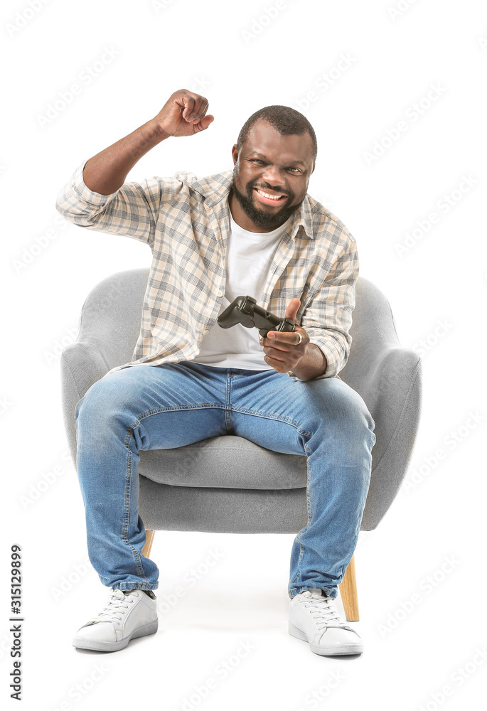 Obraz premium Emotional African-American man playing video game while sitting in armchair against white background
