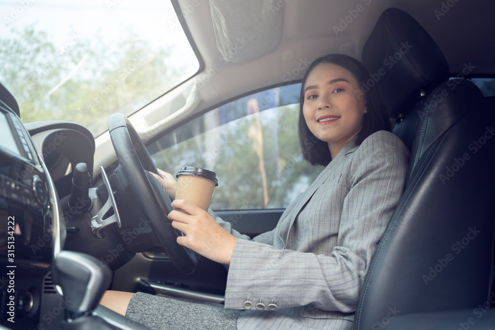 Asian female driver smiling and drinking coffee in the car, Beautiful girl holding an eco paper coffee cup,looking to camera while driving her car, happy life transport in city Asian female driver smiling and drinking coffee in the car, Beautiful girl holding an eco paper coffee cup,looking to camera while driving her car, happy life transport in city