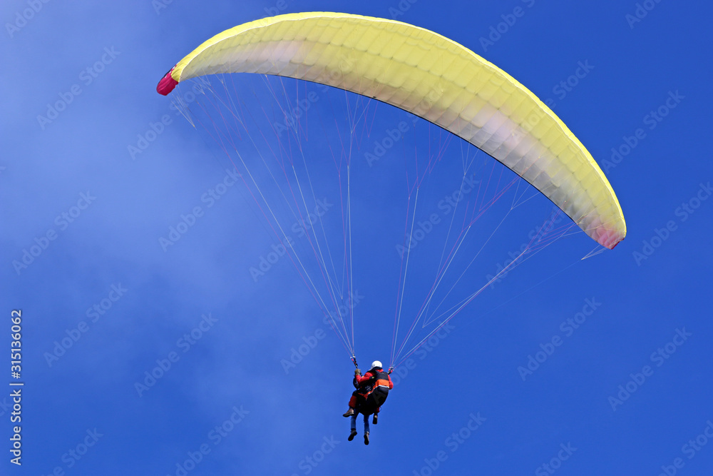 Tandem Paraglider flying wing in a blue sky Tandem Paraglider flying wing in a blue sky