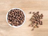 Allspice in white bowl on a brown wooden background. Indian cuisine, ayurveda, naturopathy, modern apothecary concept