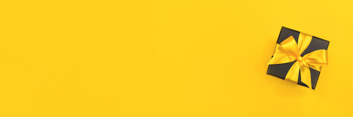 Black gift box with bow on yellow background. Flat lay. Copy space.