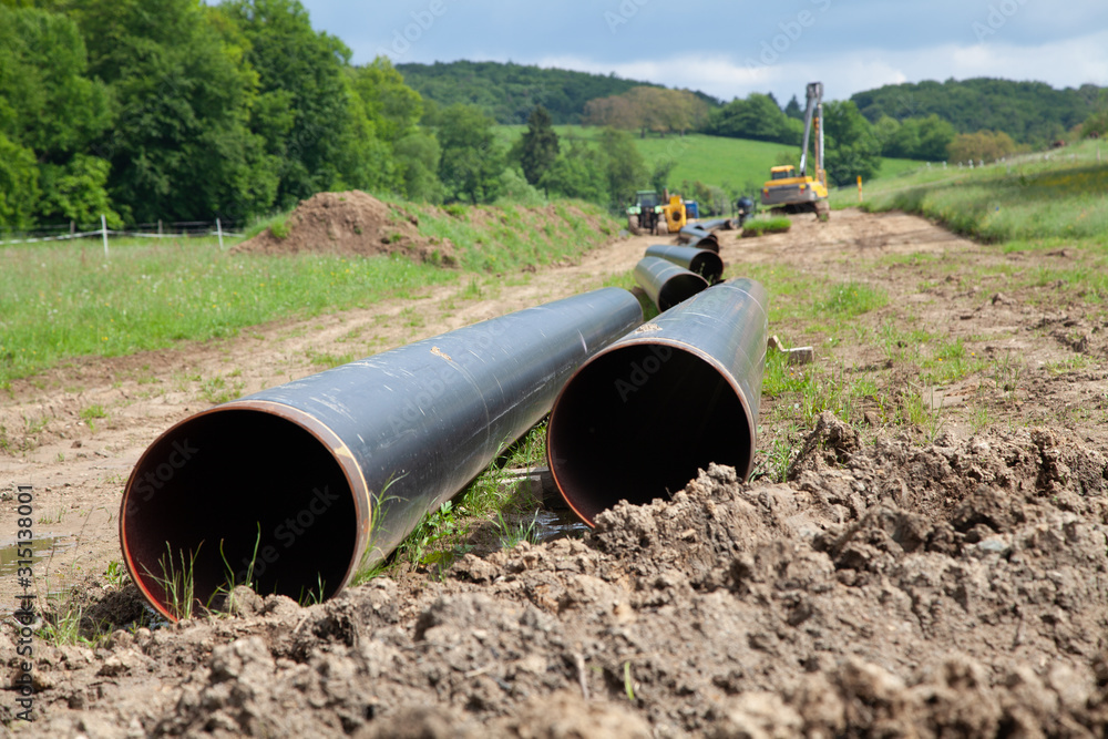 Gas pipeline laying on the countryside with two gas pipeline pipes in the foreground and machines for pipe laying along with other pipes in the background Gas pipeline laying on the countryside with two gas pipeline pipes in the foreground and machines for pipe laying along with other pipes in the background
