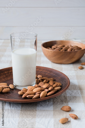 healthy food concept, almonds and glass of milk on a plate on the table