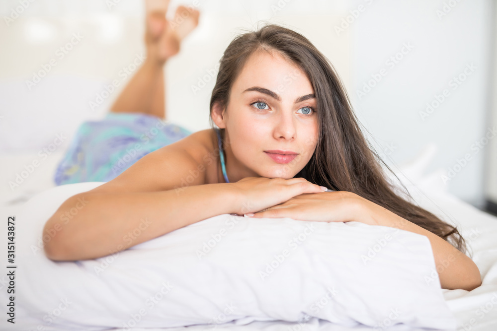 Young woman looking at camera and smiling while lying on the bed at home Young woman looking at camera and smiling while lying on the bed at home