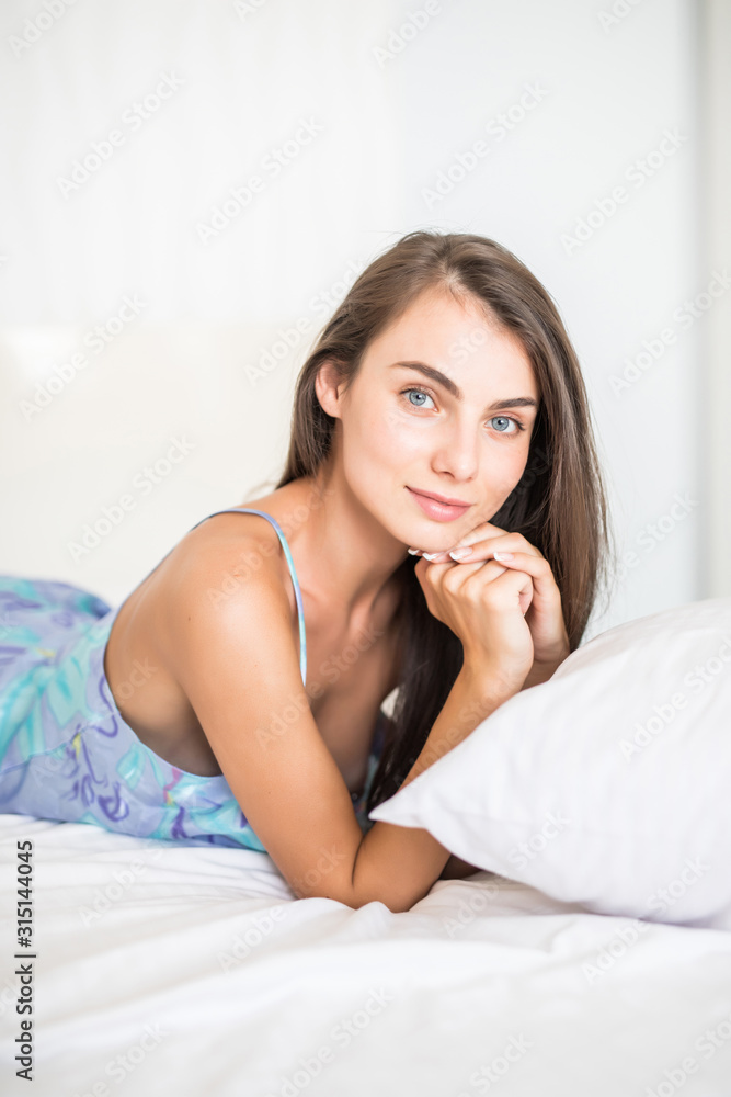 Young woman looking at camera and smiling while lying on the bed at home Young woman looking at camera and smiling while lying on the bed at home