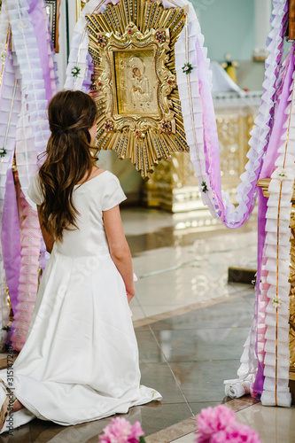 The bride is standing back on her knees near the icon in the church. Close up.