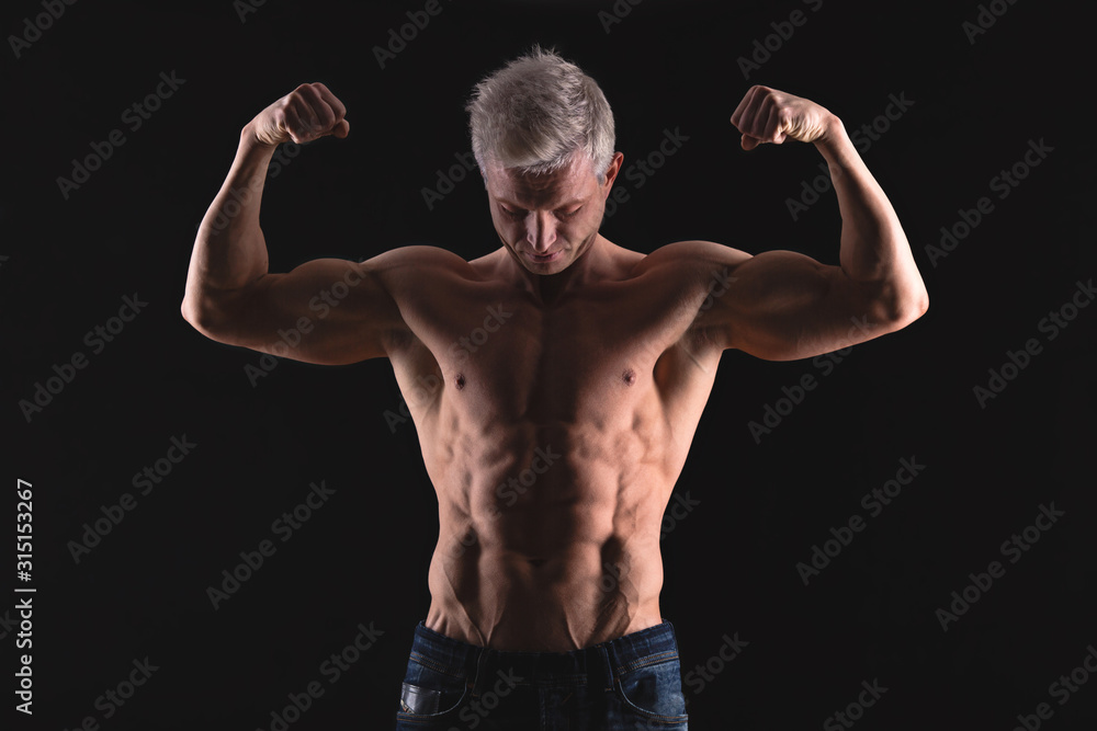 Handsome power athletic man in dramatic light. Strong bodybuilder with perfect shoulders, biceps, triceps, back, delta and chest. Strength and motivation
