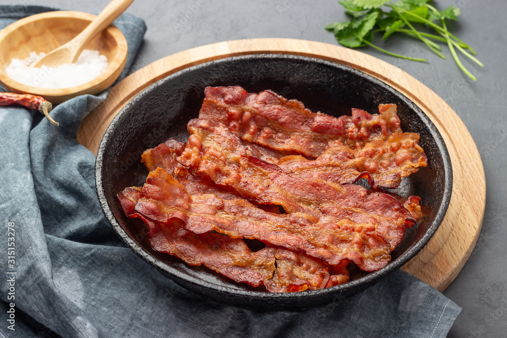 Crispy fried bacon in a cast iron pan on a gray background. Crispy fried bacon in a cast iron pan on a gray background.