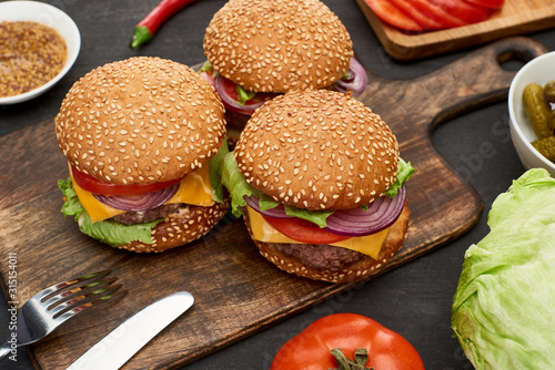 tasty fresh cheeseburgers on wooden board with cutlery