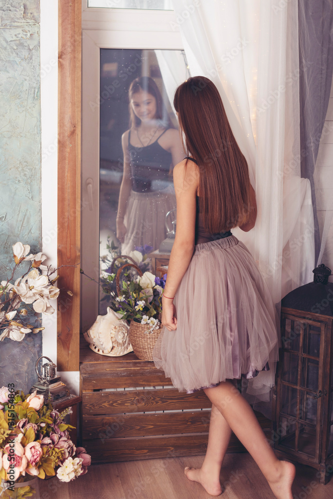 Fototapeta premium a pretty teenage brunette girl with long hair stands near the mirror, a concept of youth and natural female beauty