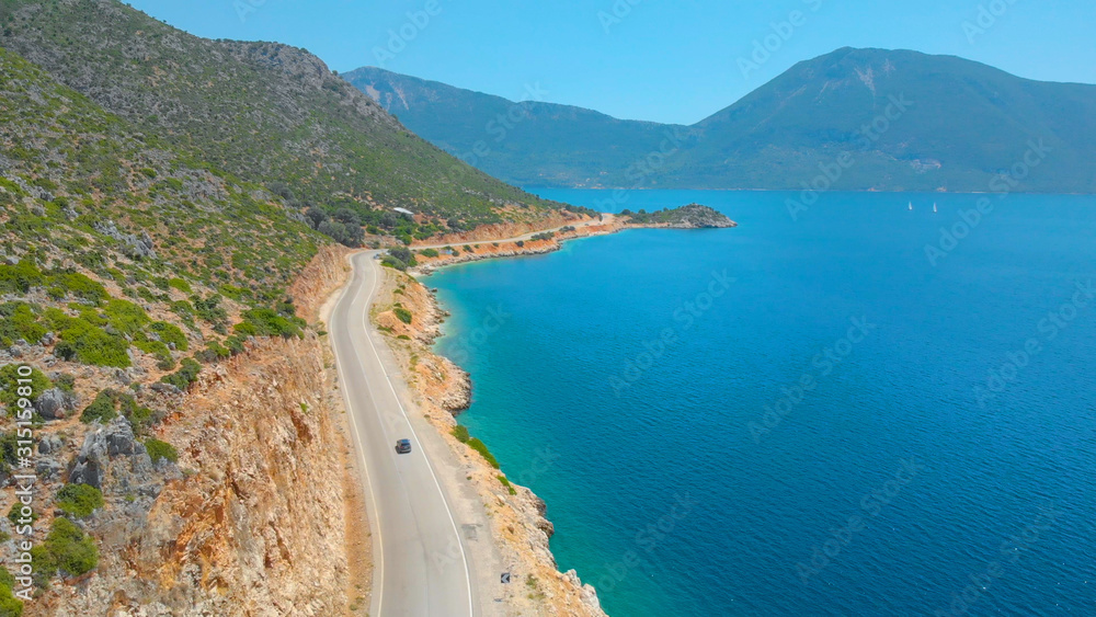 DRONE: Picturesque Mediterranean landscape surrounds car driving down the road.