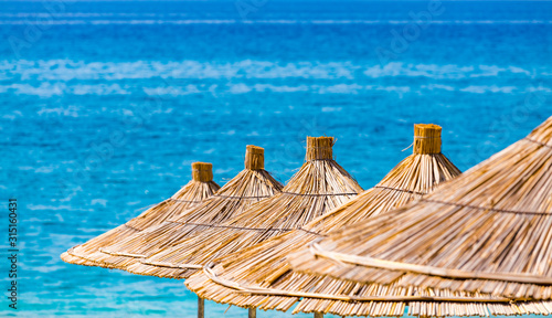 Closeup of reed beach umbrellas on a blue turquoise warm sea background. Tropical resort beach summer background. No people. Free text space.