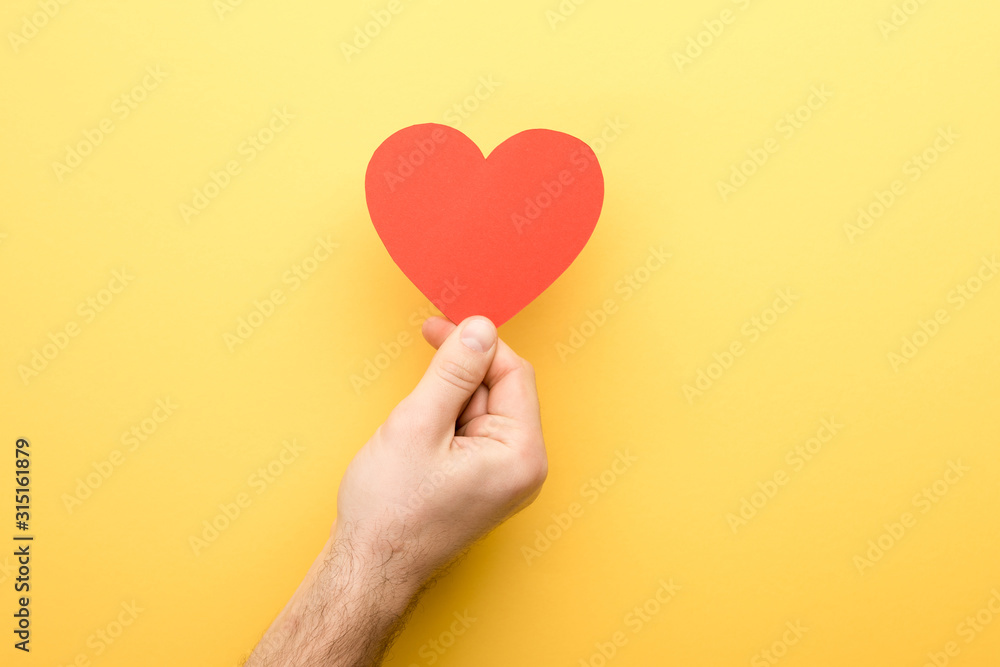 cropped view of man holding heart-shaped card on yellow background cropped view of man holding heart-shaped card on yellow background