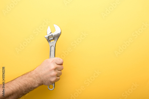 cropped view of man holding spanner on yellow background