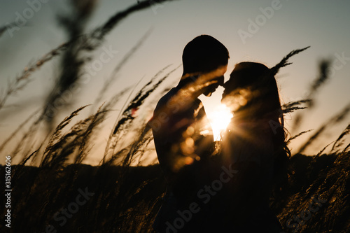Fototapeta Young couple hugging and kissing, at sunset in autumn at an outdoor on park. at the field grass on the background of sun. Concept of friendly family. upper half. Close Up. Place for text and design.