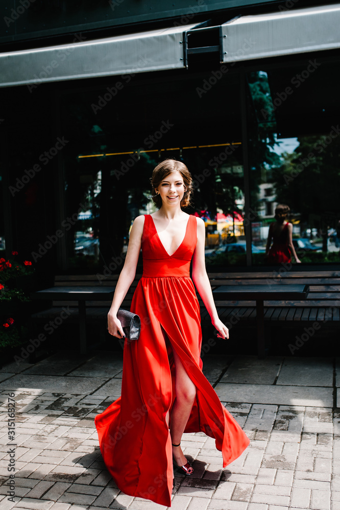 Beautiful sexy european brunette girl in evening red dress in goes near table, cafe outside, outdoors. Looking into camera happy. Poses. Whole height. Close Up. Beautiful sexy european brunette girl in evening red dress in goes near table, cafe outside, outdoors. Looking into camera happy. Poses. Whole height. Close Up.