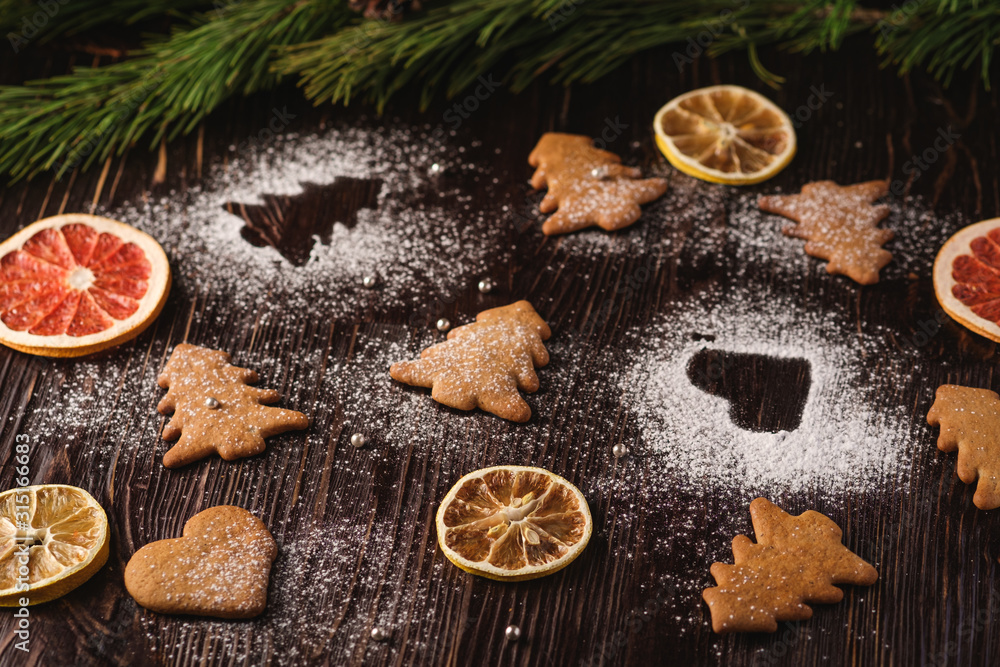 Gingerbread cookies in Christmas fir-tree and heart shape, powdered sugar on wooden background, citrus dried fruits, fir tree branch, angle view, selective focus Gingerbread cookies in Christmas fir-tree and heart shape, powdered sugar on wooden background, citrus dried fruits, fir tree branch, angle view, selective focus