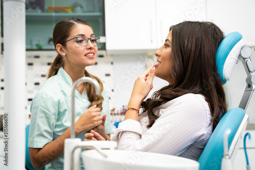 Wallpaper Mural Young woman dentist smiling at camera while her patient is sitting in a chair  Torontodigital.ca