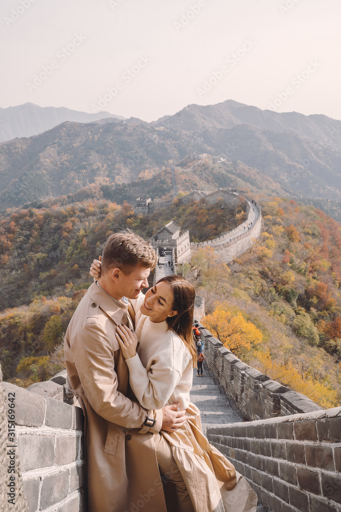 Naklejka premium beautiful young couple showing affection on the Great Wall of China. Newly married couple on their honemoon to Great Wall near Beijing China. Stylish couple exploring one of the wonders of the world