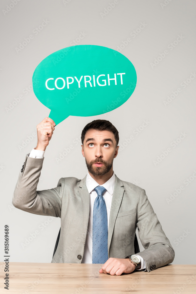 surprised businessman holding thought bubble with word copyright isolated on grey surprised businessman holding thought bubble with word copyright isolated on grey