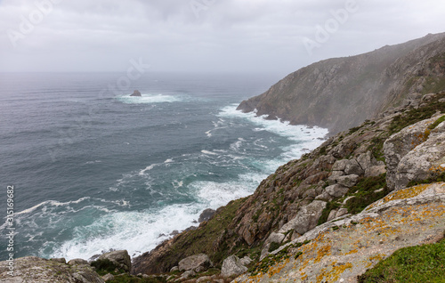 The view of the Atlantic at the end of the long pilgrim route. The cape at the Finisterre lighthouse is covered in haze. The great waves of the ocean meet the wild coast.