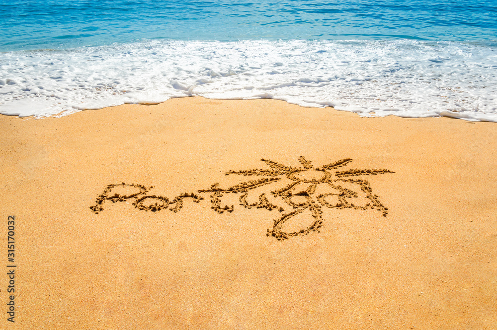 Hand written text Portugal and sun symbol on the golden beach sand with coming waves Hand written text Portugal and sun symbol on the golden beach sand with coming waves