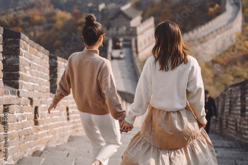 two female friends walking along the Great Wall of China near the Beijing entarnce. Two stylish girls exploring chinese culture together. Two girls holding hands dressed in matching outfits. photo