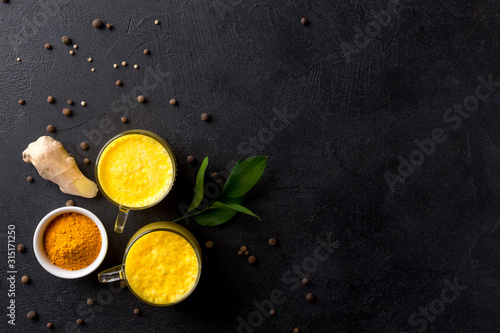 Two cups of golden latte with ginger root and turmeric on a black background.