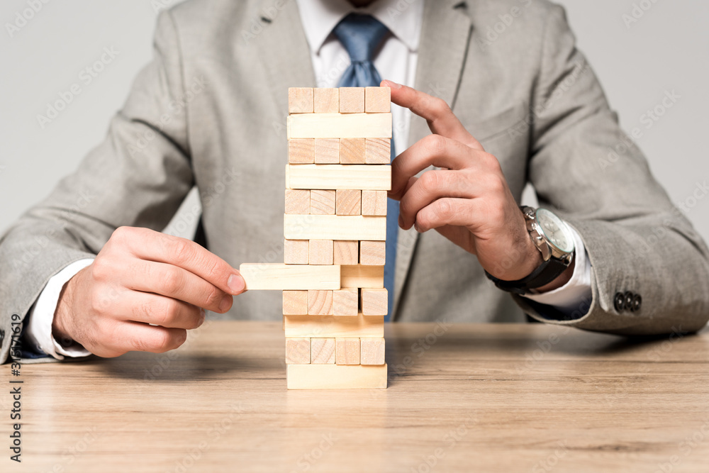 cropped view of businessman playing blocks wood tower game isolated on grey cropped view of businessman playing blocks wood tower game isolated on grey