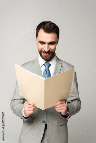 smiling businessman reading documents in paper folder isolated on grey © LIGHTFIELD STUDIOS