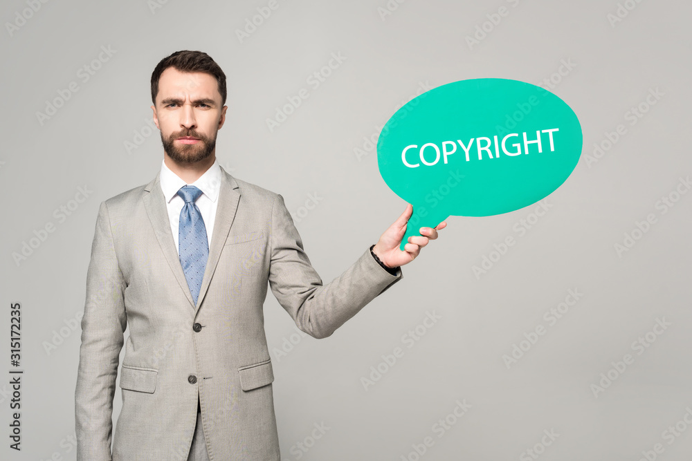 confident businessman holding thought bubble with copyright inscription isolated on grey confident businessman holding thought bubble with copyright inscription isolated on grey