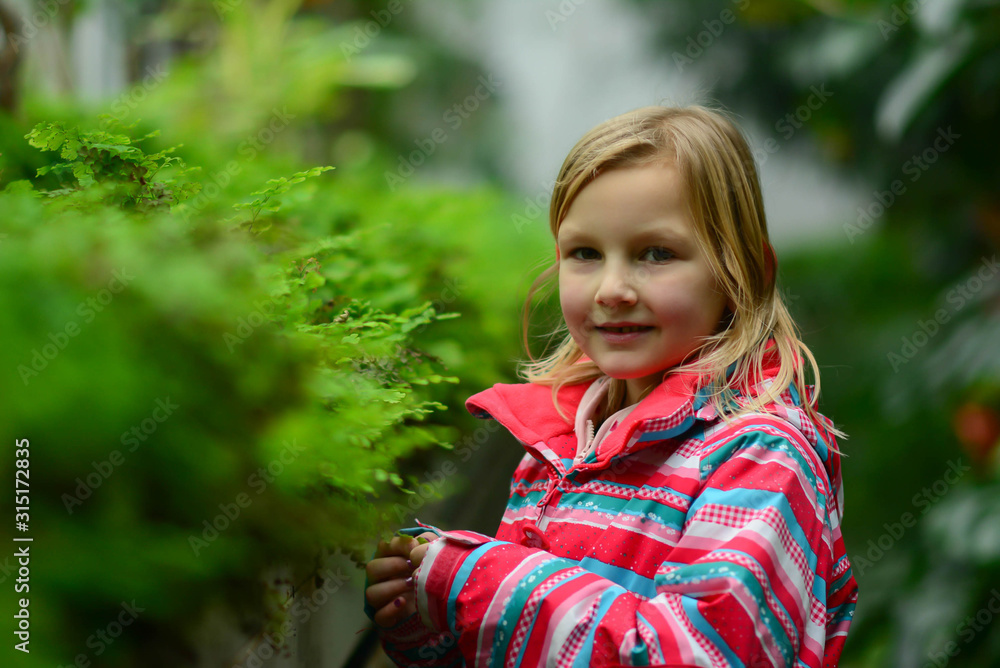 Beautiful smiling cute preschool girl in greenhouse. Beautiful expressive adorable happy cute laughing smiling girl in secret garden. Children, people, preschool and greenhouse concept Beautiful smiling cute preschool girl in greenhouse. Beautiful expressive adorable happy cute laughing smiling girl in secret garden. Children, people, preschool and greenhouse concept