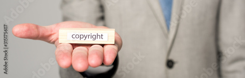 partial view of businessman showing wooden block with word copyright isolated on grey, panoramic shot