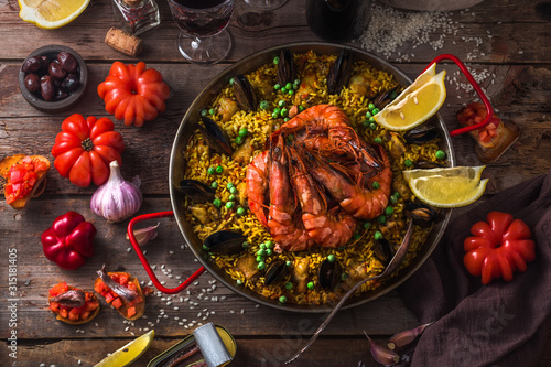 Top view of paella with prawns, mussels and lemon, wooden background