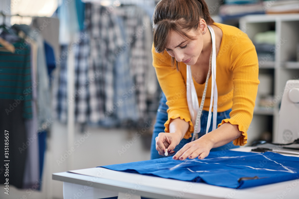 Creative caucasian fashion designer standing in her studio and drawing scheme on blue linen for a beautiful evening dress. Creative caucasian fashion designer standing in her studio and drawing scheme on blue linen for a beautiful evening dress.