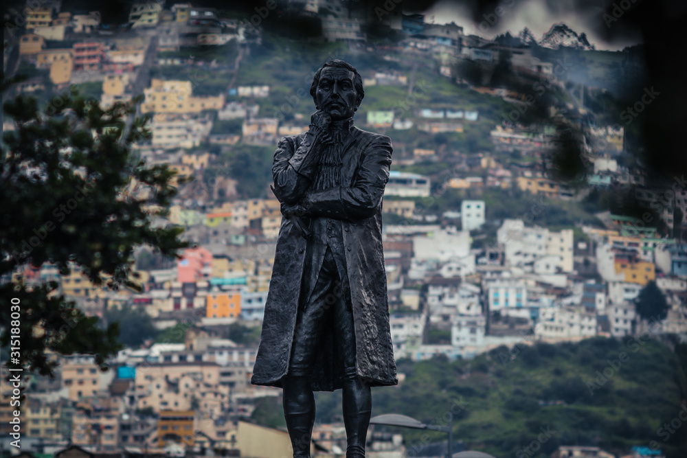 Statue on boulevard 24 de mayo square in Quito, Ecuador on a february midday. Houses of quito are seen in the distance in the background. Statue on boulevard 24 de mayo square in Quito, Ecuador on a february midday. Houses of quito are seen in the distance in the background.